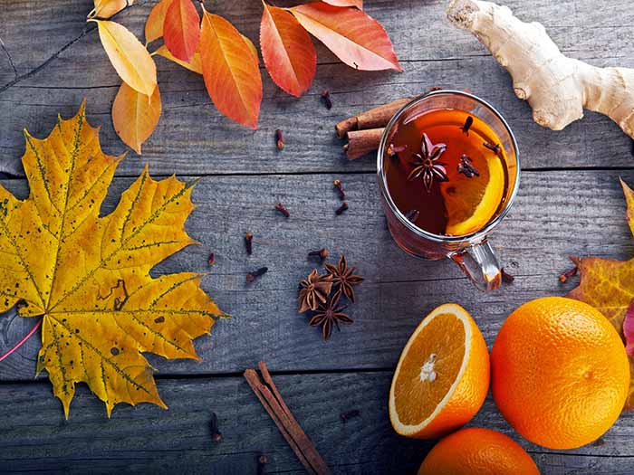Oranges and cloves on a black counter with autumn leaves next to a clove tea cup