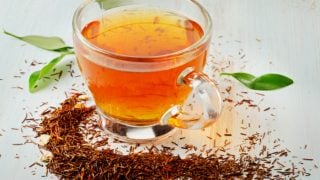 A cup of rooibos tea and loose leaves on a white table