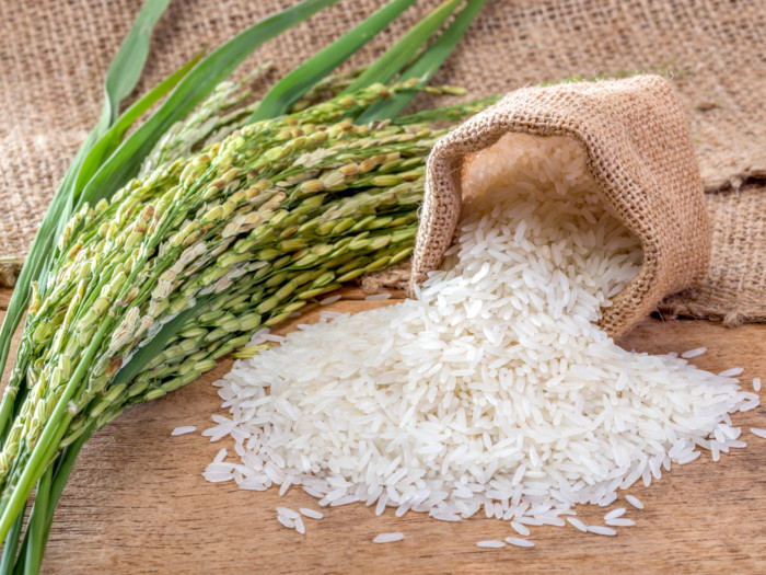 Fresh rice sprig and a small sack of white rice falling on a wooden table