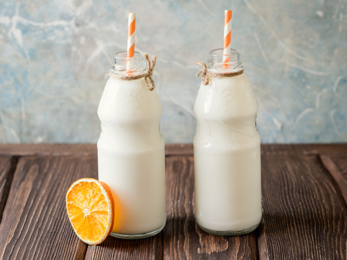 2 bottles fresh skimmed milk with orange striped straws and a slice of lime kept on a wooden table